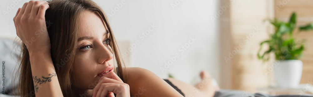 pretty and dreamy woman with tattooed hand looking away in bedroom, banner. pretty and dreamy woman with tattooed hand looking away in bedroom, banner.