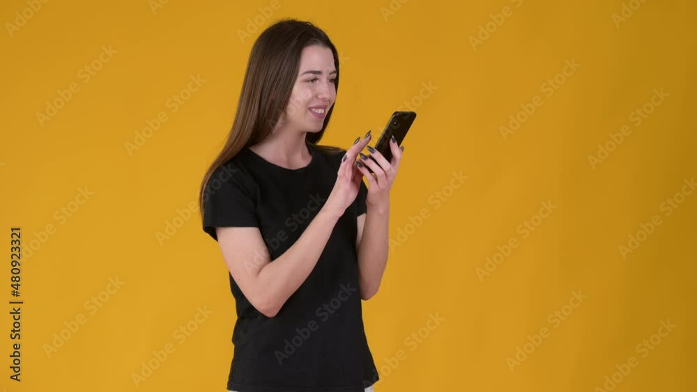 Young Happy girl using smart phone and texting online chat with smile isolated on yellow background. People lifestyle concept. Young Happy girl using smart phone and texting online chat with smile isolated on yellow background. People lifestyle concept.