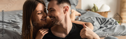 young and happy couple smiling while looking at each other in bedroom, banner.
