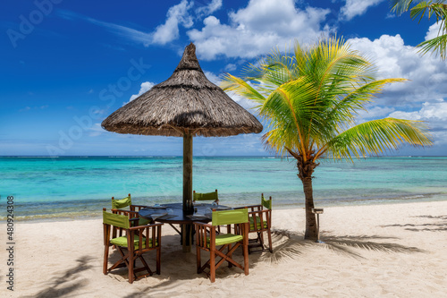 Beach cafe on sandy beach under straw umbrella  palm trees and beautiful sea on exotic tropical island.