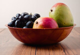 Fresh mango and dark grapes in a small wooden bowl and table. Still life. Light and rich saturated color.