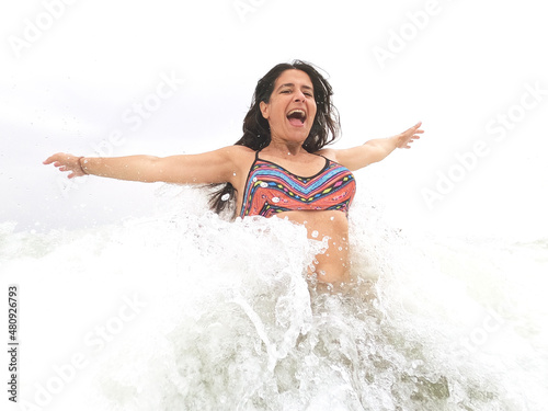 Beautiful attractive brunette woman happy in bikini jumping sea waves