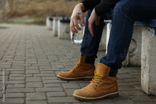 Addicted man with alcoholic drink on bench outdoors, closeup. Space for text