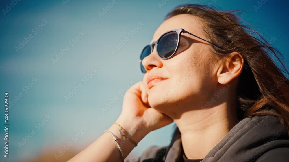 Portrait of a young adult woman wearing sunglasses enjoying the fresh air on the backdrop of the blue sky Portrait of a young adult woman wearing sunglasses enjoying the fresh air on the backdrop of the blue sky