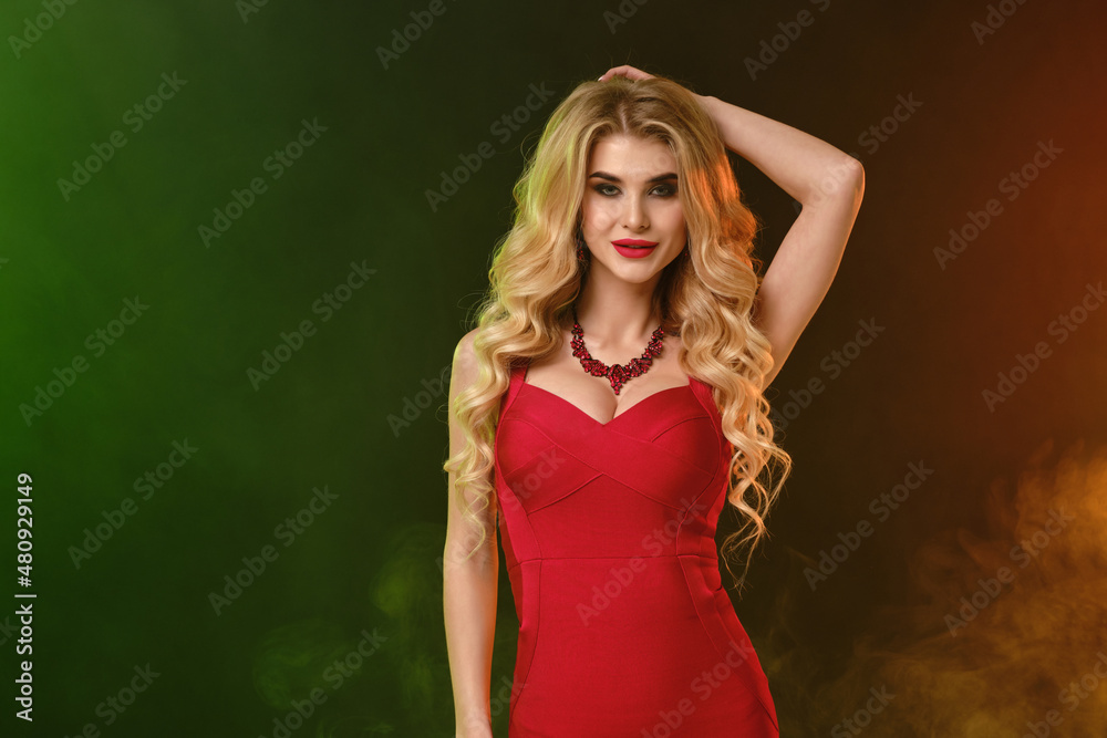 Blonde lady with bright make-up, in red fitting dress and necklace. Smiling, posing on colorful smoky studio background. Fashion and beauty. Close up Blonde lady with bright make-up, in red fitting dress and necklace. Smiling, posing on colorful smoky studio background. Fashion and beauty. Close up