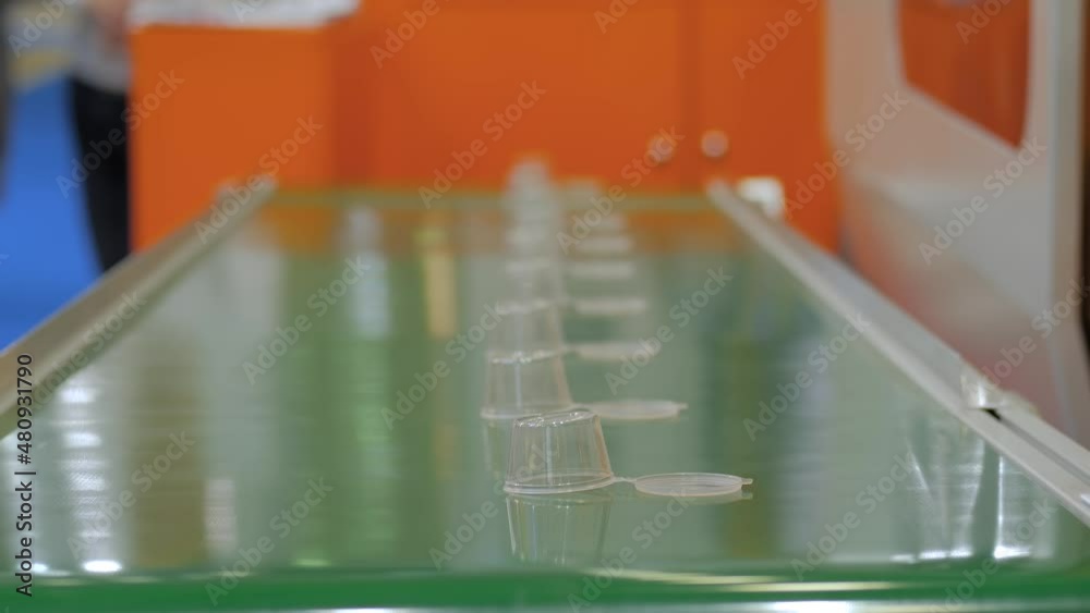Close up: conveyor belt with moving empty plastic sauce cups at factory, exhibition. Manufacturing, recycling, industry, technology concept Close up: conveyor belt with moving empty plastic sauce cups at factory, exhibition. Manufacturing, recycling, industry, technology concept