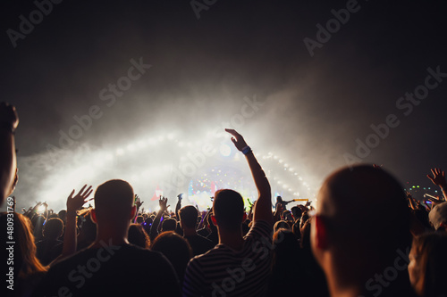 Young people having fun at a music festival. A lot of people standing and dancing in front of a concert stage.