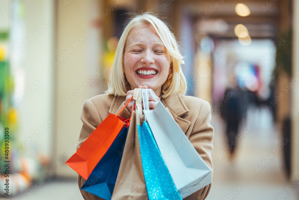 Happiness, consumerism, sale and people concept - smiling young woman with shopping bags over mall background. Portrait of young happy smiling woman with shopping bags Happiness, consumerism, sale and people concept - smiling young woman with shopping bags over mall background. Portrait of young happy smiling woman with shopping bags
