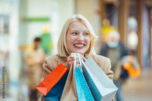 Happiness, consumerism, sale and people concept - smiling young woman with shopping bags over mall background. Portrait of young happy smiling woman with shopping bags