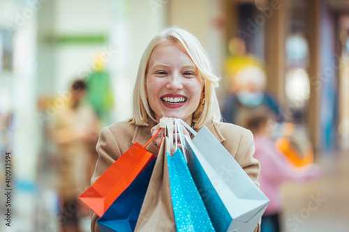 Happiness, consumerism, sale and people concept - smiling young woman with shopping bags over mall background. Portrait of young happy smiling woman with shopping bags