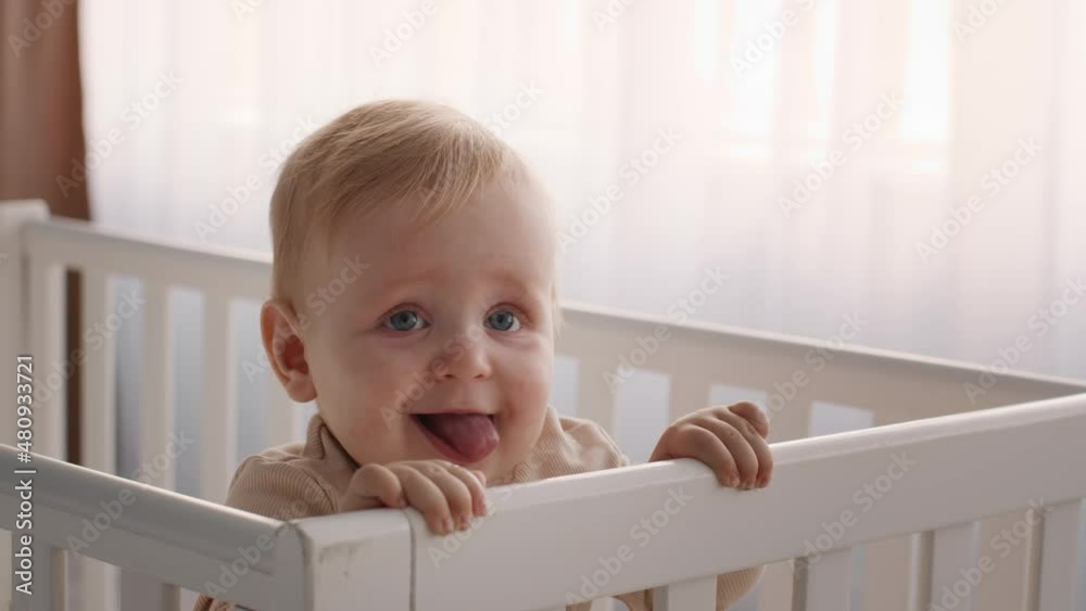 Closeup Shot Of Adorable Infant Baby Standing In His Crib And Grimacing Closeup Shot Of Adorable Infant Baby Standing In His Crib And Grimacing