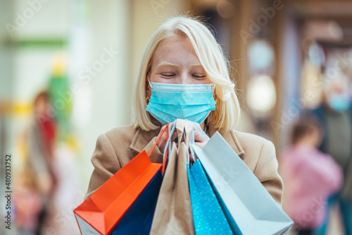 Beautiful girl shopper in medical face mask holding shopping bags in hands. Young happy woman customer in protective mask on face with paper bags. Girl shopaholic. Coronavirus COVID-19, sale, discount