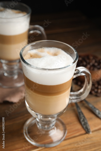 Delicious latte macchiato and coffee beans on wooden table