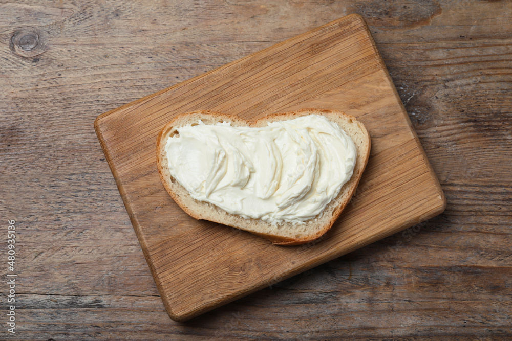 Slice of bread with tasty cream cheese on wooden table, top view Slice of bread with tasty cream cheese on wooden table, top view