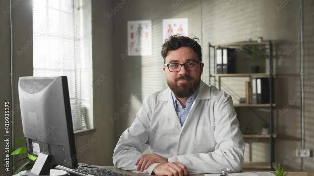 Medium shot european doctor in the office using PC. Indoor portrait smiling confident family therapist in white gown at work. Medium shot european doctor in the office using PC. Indoor portrait smiling confident family therapist in white gown at work.