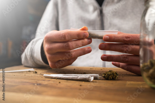 Canvas Print Man rolling marijuana cannabis joint in coffee shop Amsterdam with CBD weed buds in glass jars