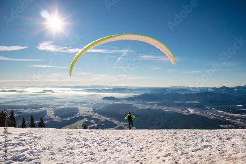 Paragliding in mountains, winter time with snow and blue sunny sky.