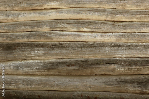 The wall of an old wooden house made of darkened weathered logs. Texture of old vintage wooden planks background natural.