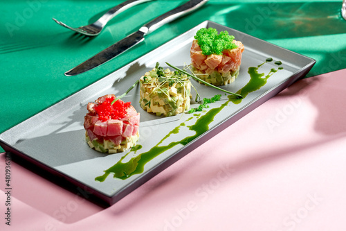 Tartar with tuna, avocado and white sauce in a gray plate. Colored backgrounds. Hard light. selective focus