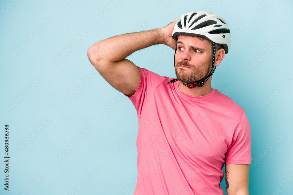 Young caucasian man with bike helmet isolated on blue background touching back of head, thinking and making a choice.