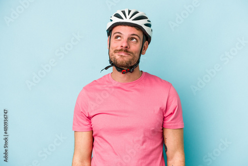 Young caucasian man with bike helmet isolated on blue background dreaming of achieving goals and purposes