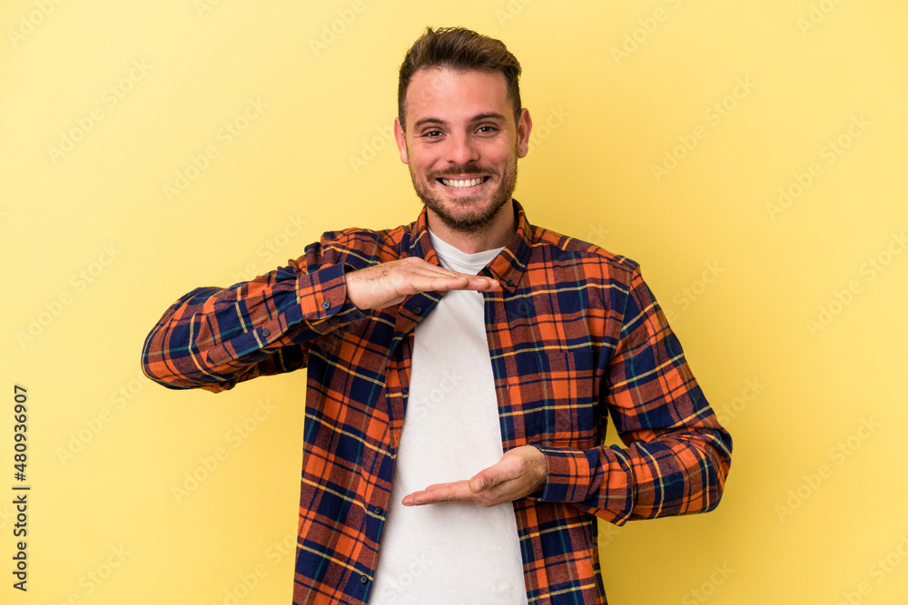 Young caucasian man isolated on yellow background holding something with both hands, product presentation. Young caucasian man isolated on yellow background holding something with both hands, product presentation.