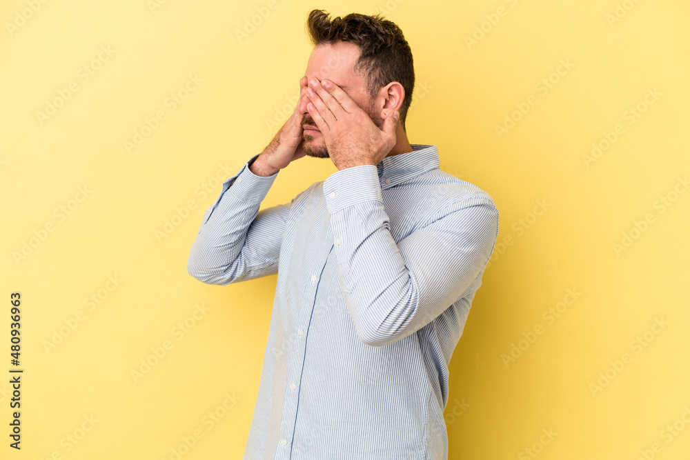 Young caucasian man isolated on yellow background afraid covering eyes with hands. Young caucasian man isolated on yellow background afraid covering eyes with hands.