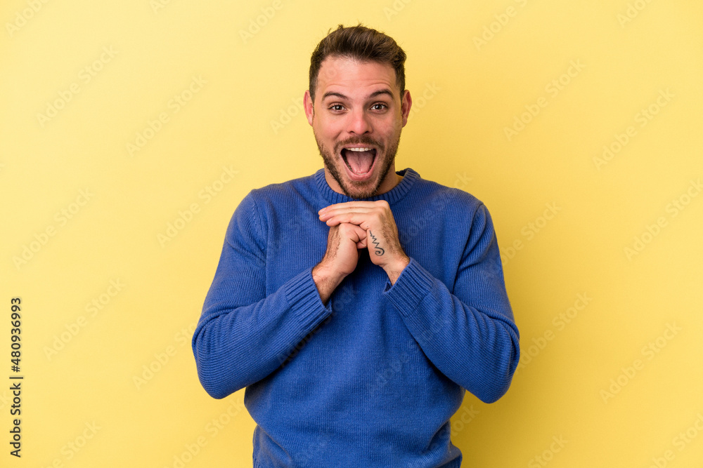 Young caucasian man isolated on yellow background praying for luck, amazed and opening mouth looking to front. Young caucasian man isolated on yellow background praying for luck, amazed and opening mouth looking to front.