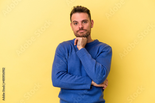 Young caucasian man isolated on yellow background suspicious, uncertain, examining you.