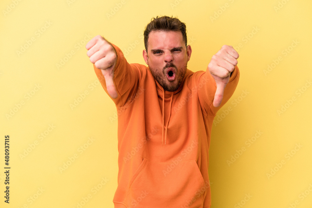 Young caucasian man isolated on yellow background showing thumb down and expressing dislike.