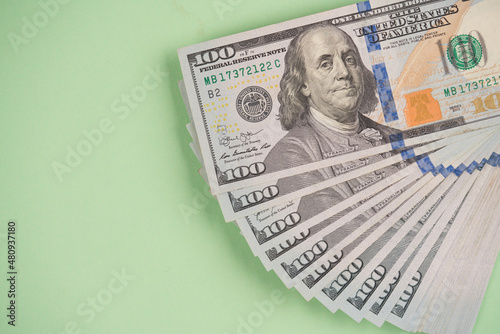 Stack of one hundred dollars banknotes on light green background with copy space. Cash money. Financial growth and business concept