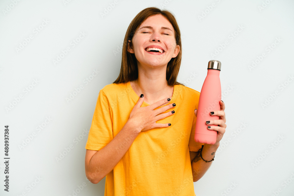 Young English woman holding a thermo isolated on blue background laughs out loudly keeping hand on chest. Young English woman holding a thermo isolated on blue background laughs out loudly keeping hand on chest.