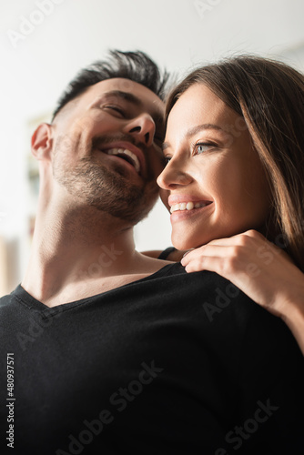 low angle view of happy young woman embracing laughing boyfriend in bedroom.