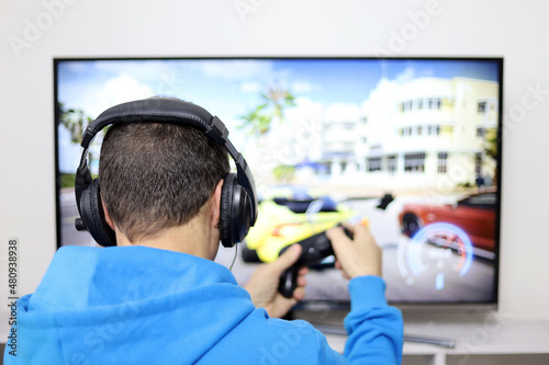 Guy in headphones playing with a gamepad a racing video game on TV screen. Concept of game addiction, home leisure