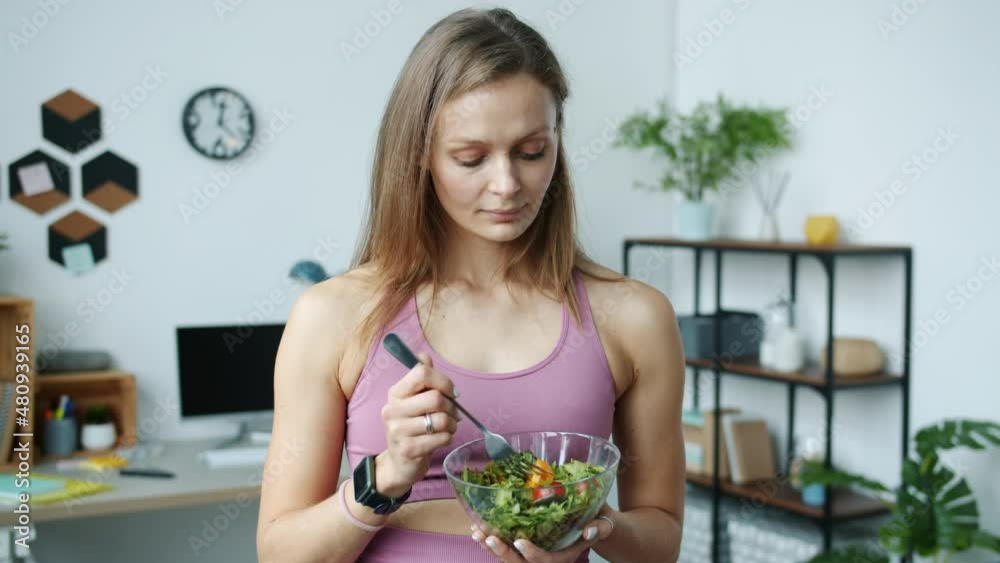 Slow motion portrait of attractive girl holding bowl of salad standing at home enjoying vegetables smiling looking at camera. People and nutrition concept. Slow motion portrait of attractive girl holding bowl of salad standing at home enjoying vegetables smiling looking at camera. People and nutrition concept.