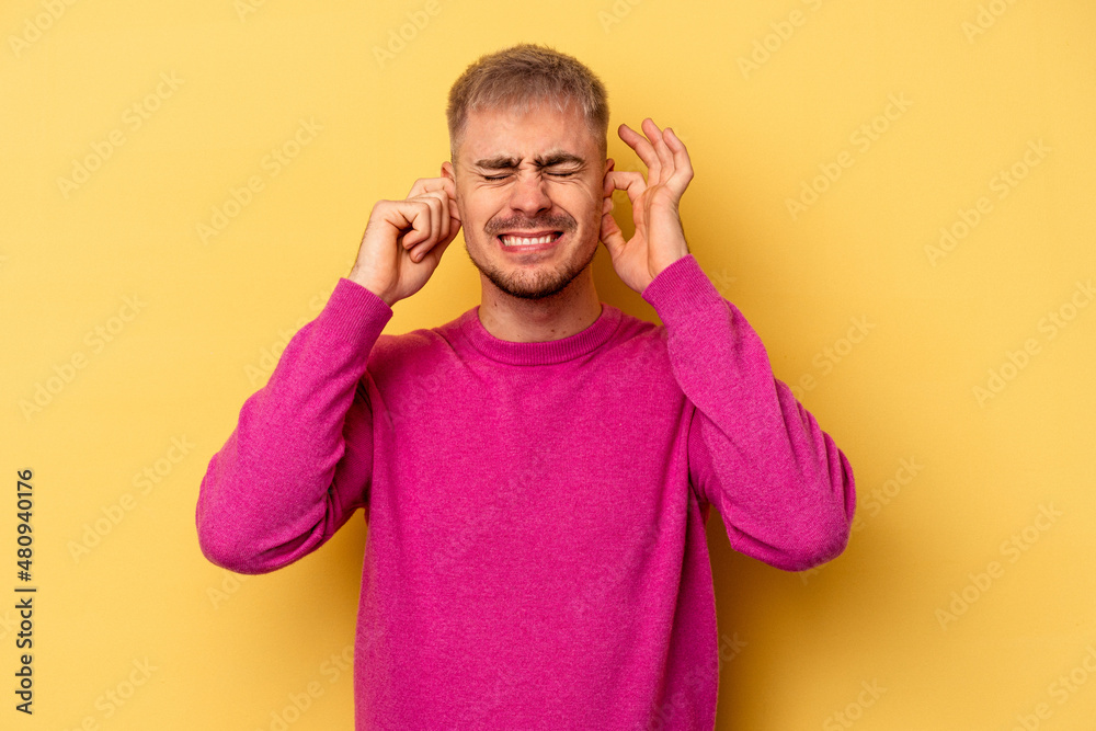 Young caucasian man isolated on yellow background covering ears with hands. Young caucasian man isolated on yellow background covering ears with hands.