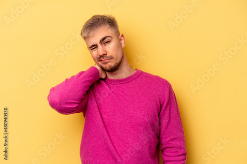 Young caucasian man isolated on yellow background having a neck pain due to stress, massaging and touching it with hand. © Asier
