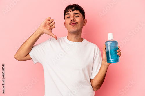 Young mixed race man holding mouthwash isolated on pink background feels proud and self confident, example to follow.