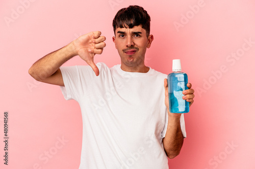 Young mixed race man holding mouthwash isolated on pink background showing a dislike gesture, thumbs down. Disagreement concept.
