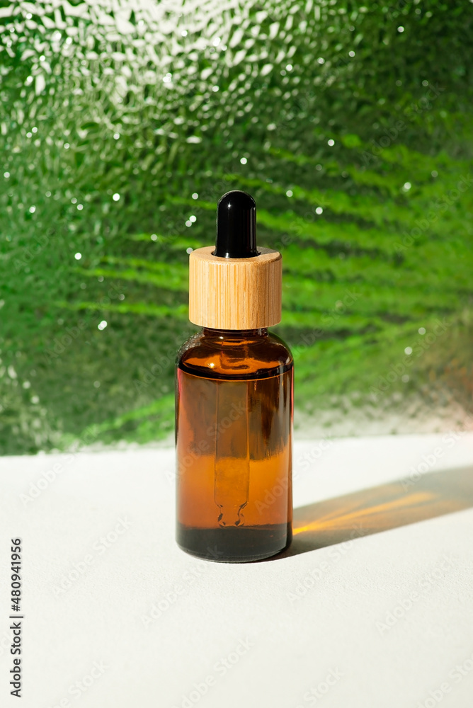 Amber glass bottle with dropper pipette with serum or essential oil against the background of corrugated glass. Skincare cosmetic with palm leaves. Beauty concept for face body care