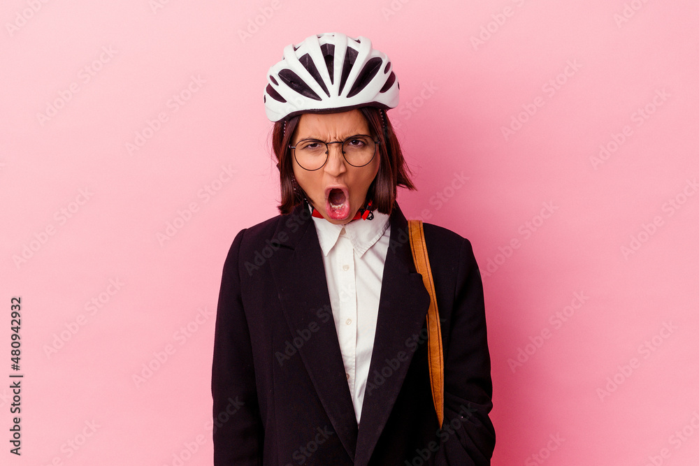 Young business mixed race woman wearing a bike helmet isolated on pink background screaming very angry and aggressive. Young business mixed race woman wearing a bike helmet isolated on pink background screaming very angry and aggressive.