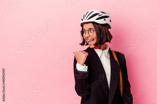 Young business mixed race woman wearing a bike helmet isolated on pink background points with thumb finger away, laughing and carefree.