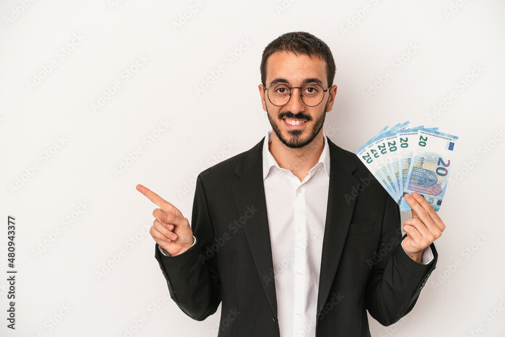 Young caucasian business man holding banknotes isolated on white background smiling and pointing aside, showing something at blank space. Young caucasian business man holding banknotes isolated on white background smiling and pointing aside, showing something at blank space.