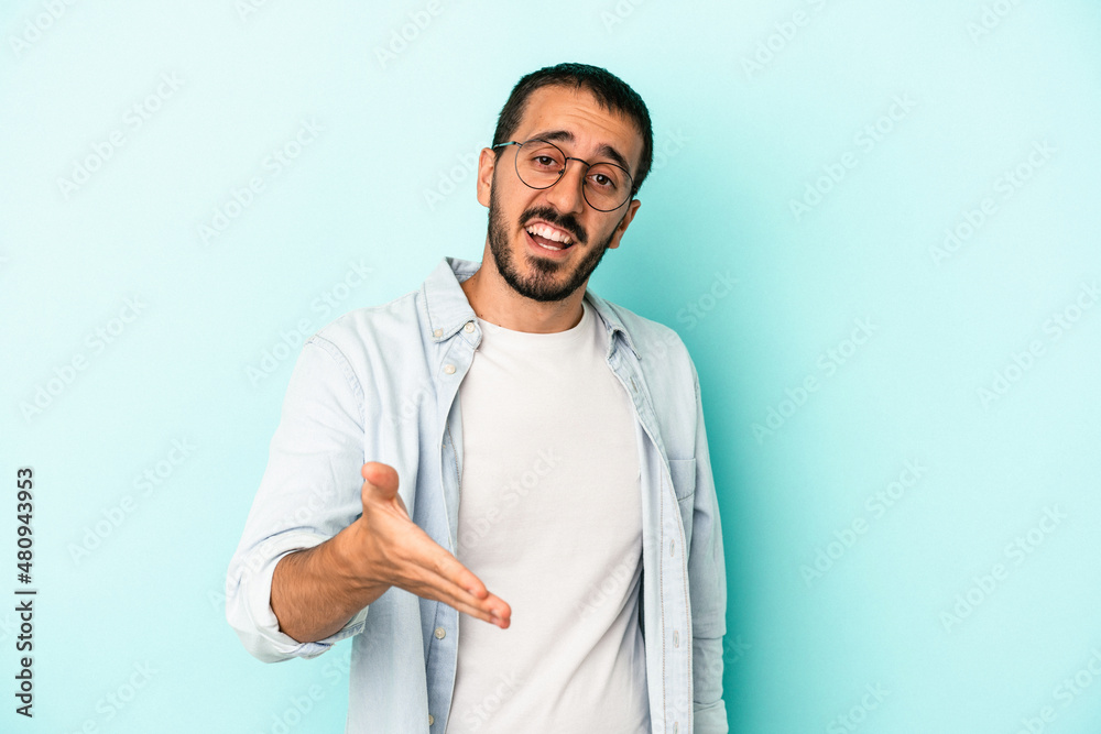 Young caucasian man isolated on blue background stretching hand at camera in greeting gesture. Young caucasian man isolated on blue background stretching hand at camera in greeting gesture.