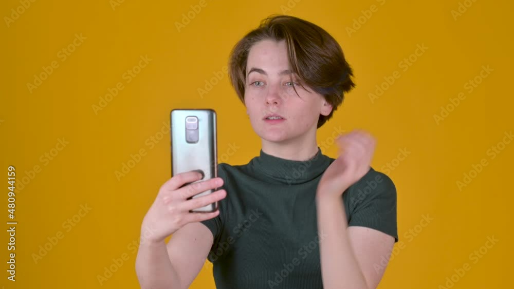 Young brunette girl posing doing selfie shot on mobile cell phone video call isolated on yellow studio background. people lifestyle concept Young brunette girl posing doing selfie shot on mobile cell phone video call isolated on yellow studio background. people lifestyle concept