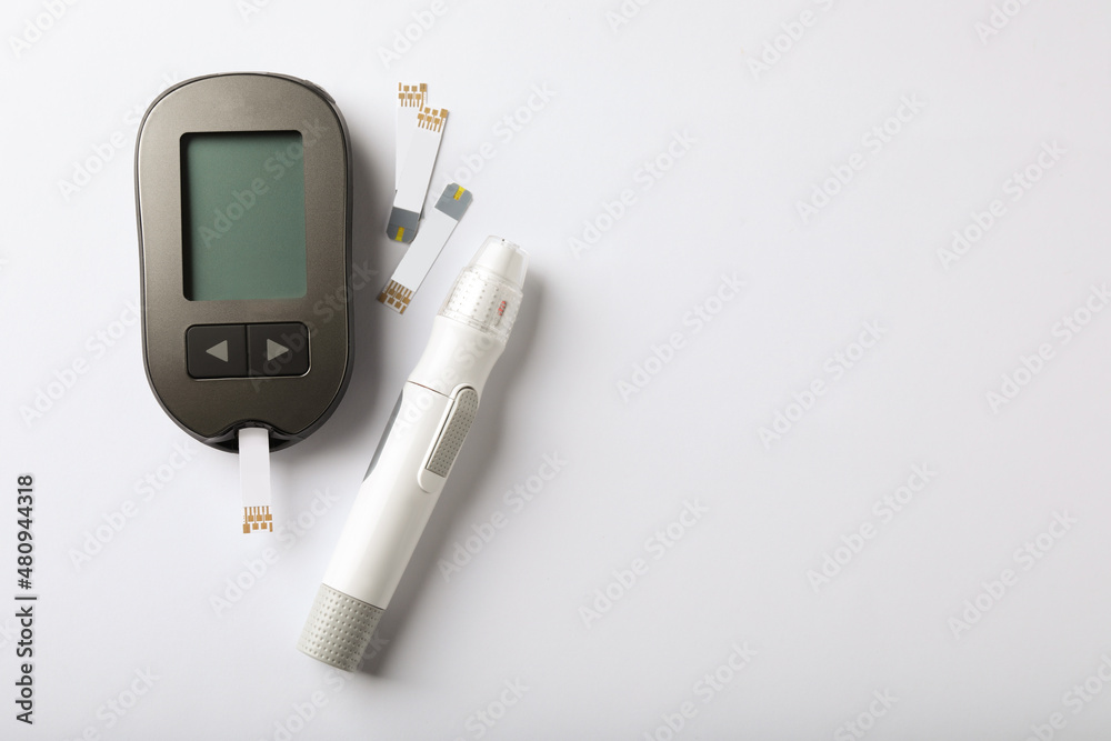 Digital glucometer, lancet pen and test strips on white background, flat lay with space for text. Diabetes control Digital glucometer, lancet pen and test strips on white background, flat lay with space for text. Diabetes control