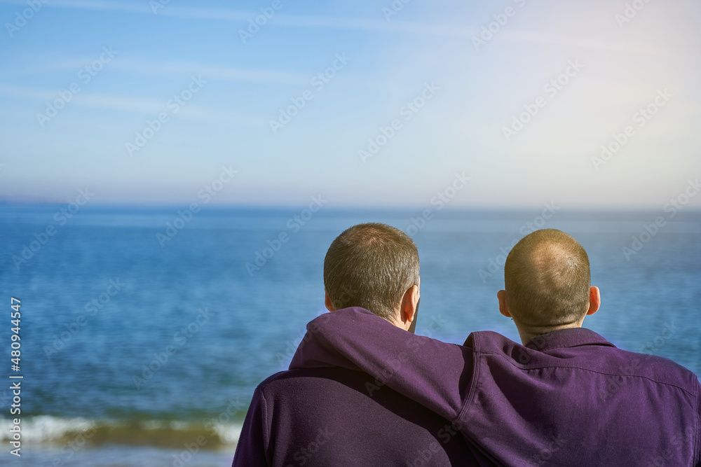 Father's day love concept. Son puts arm around father's back at the beach on a sunny day