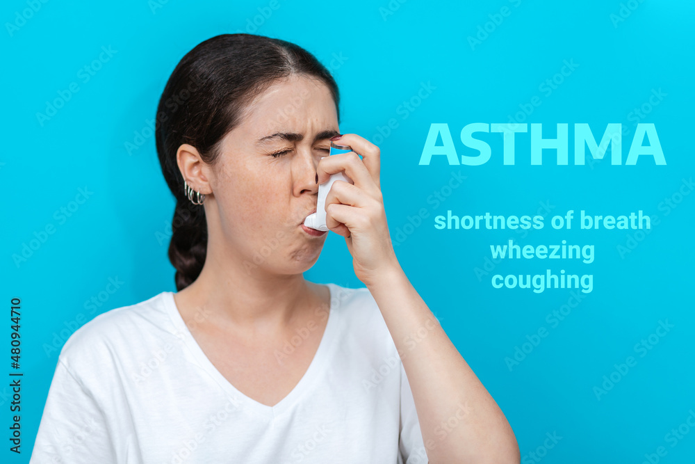 Symptoms of asthma. Portrait of a young woman wincing when using an inhaler. Blue background. Text Symptoms of asthma. Portrait of a young woman wincing when using an inhaler. Blue background. Text