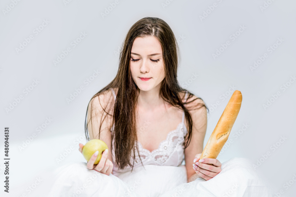 Breakfast in bed. Healthy lifestyle or calories. A woman sits on the bed and chooses what to eat a baguette or an apple. Morning Breakfast in bed. Healthy lifestyle or calories. A woman sits on the bed and chooses what to eat a baguette or an apple. Morning