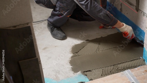 Spreading wet mortar before applying tiles on bathroom floor. puts adhesive. Applying tile adhesive to the floor.
